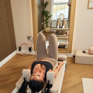 A client lying on a pilates reformer with their head positioned centrally on the apparatus in a light, modern studio.
