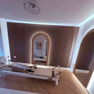 The reformer in Nicola's Harrogate studio, with warm wood flooring, ribbed wall panelling and a gold archway behind it.